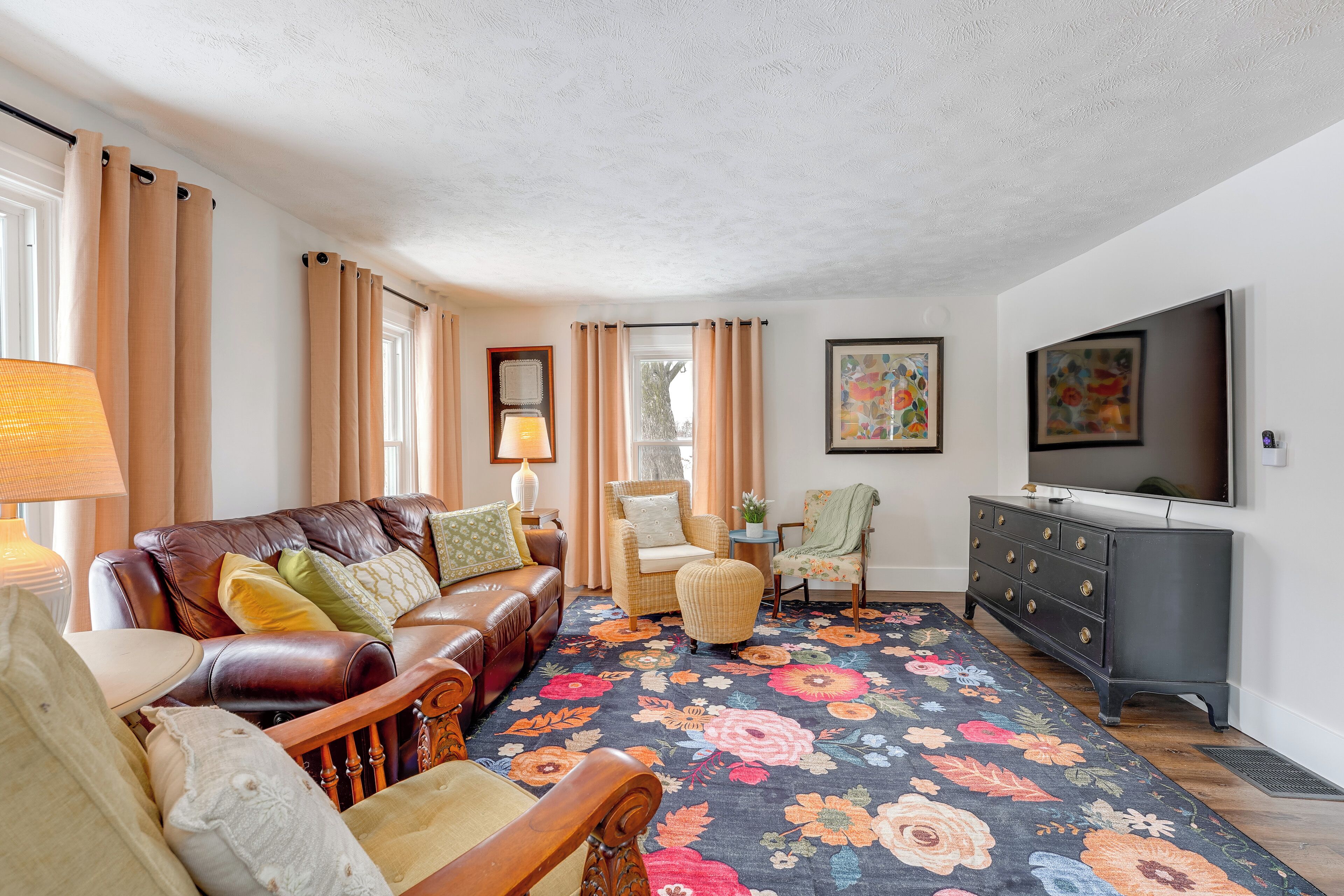 A living room with a brown leather sofa, a wooden chair, a small table, a TV, and a floral rug.