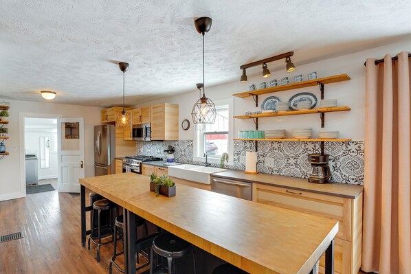 Una cocina moderna con encimeras de madera, electrodomésticos de acero inoxidable y estantes decorativos.