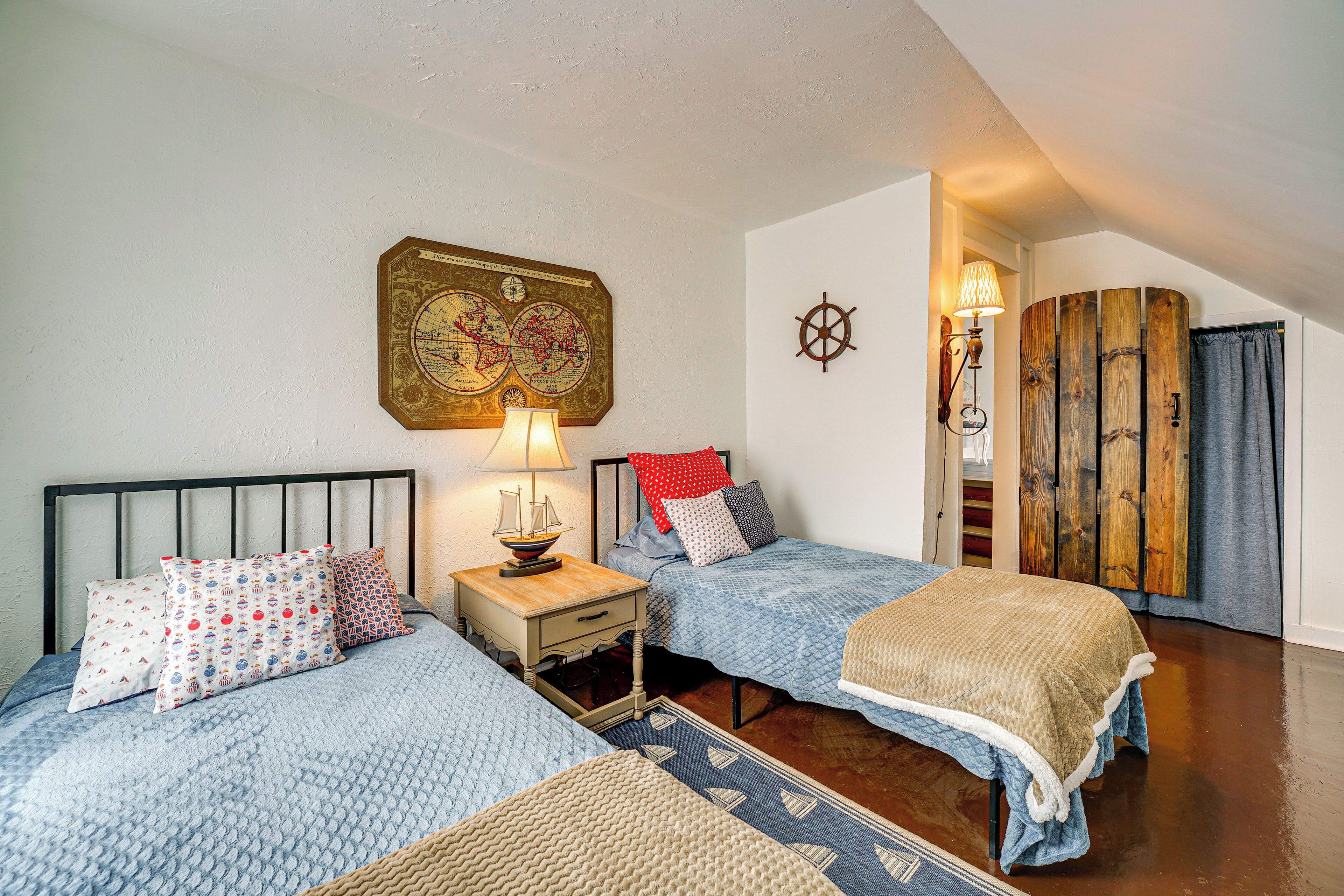 A bedroom with two beds, a wooden headboard, a map on the wall, and a ship-shaped lamp.
