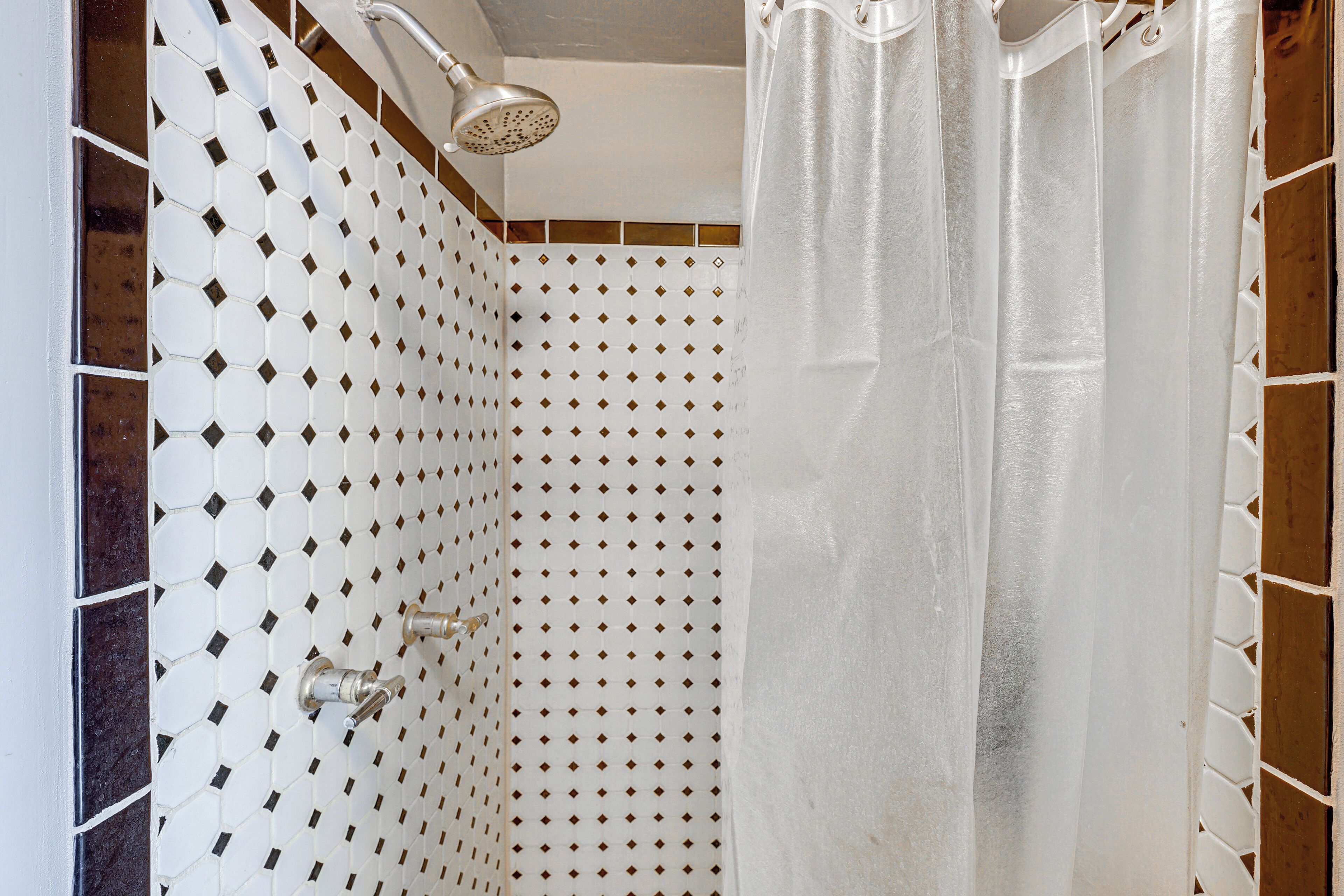 A shower with a white tiled wall, a showerhead, and a curtain.