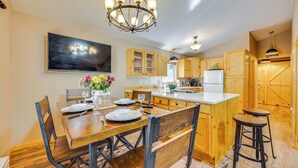 A modern kitchen with wooden cabinets, a central island, bar stools, and a chandelier.