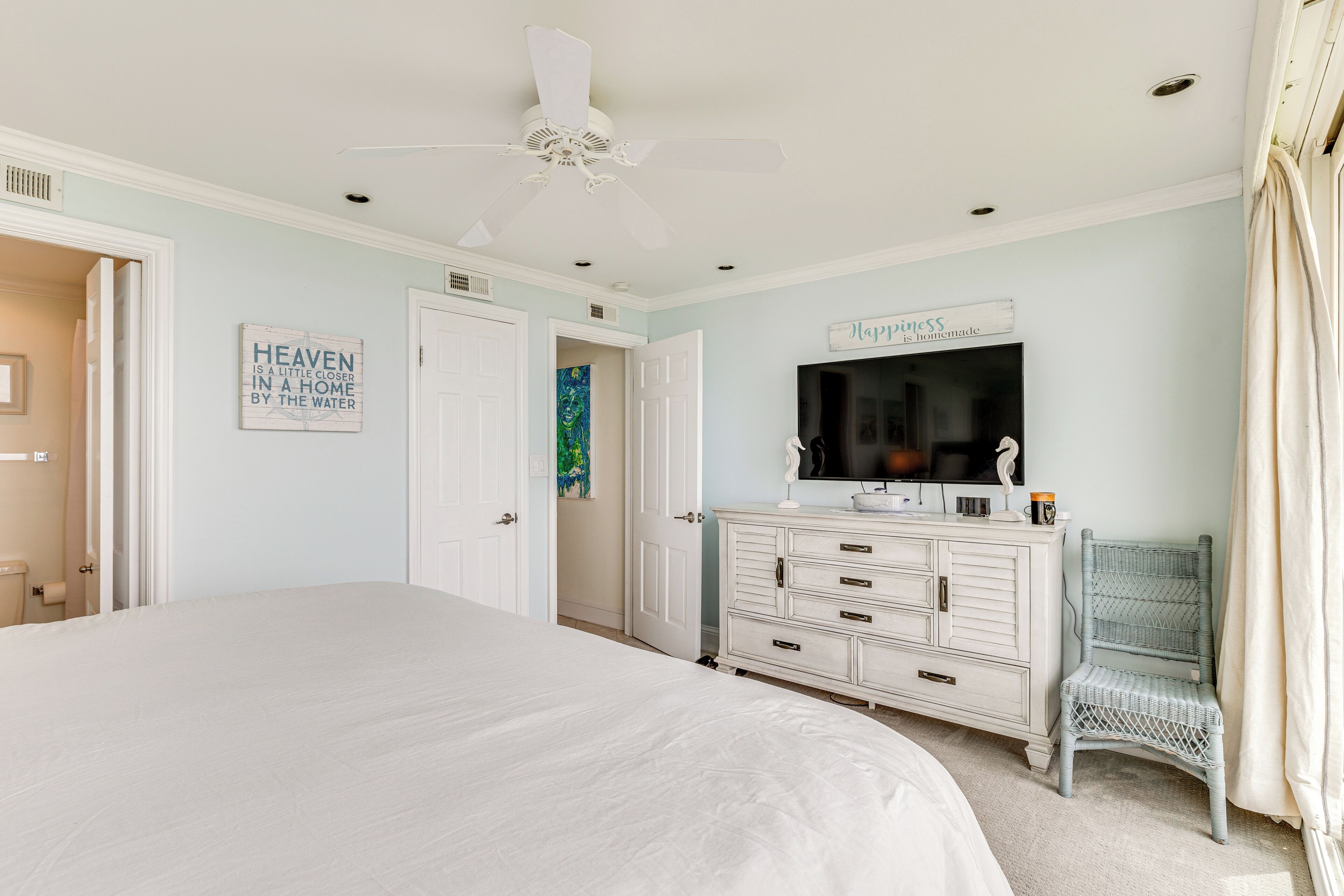A bedroom with a large bed, a dresser, a chair, and a ceiling fan.