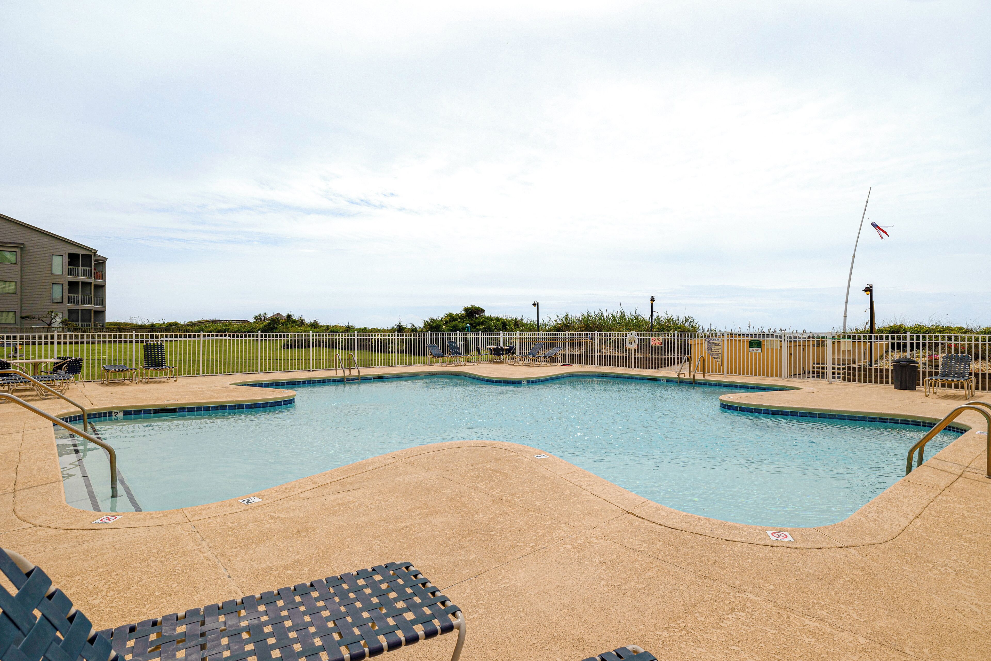 A swimming pool with lounge chairs and a flagpole.