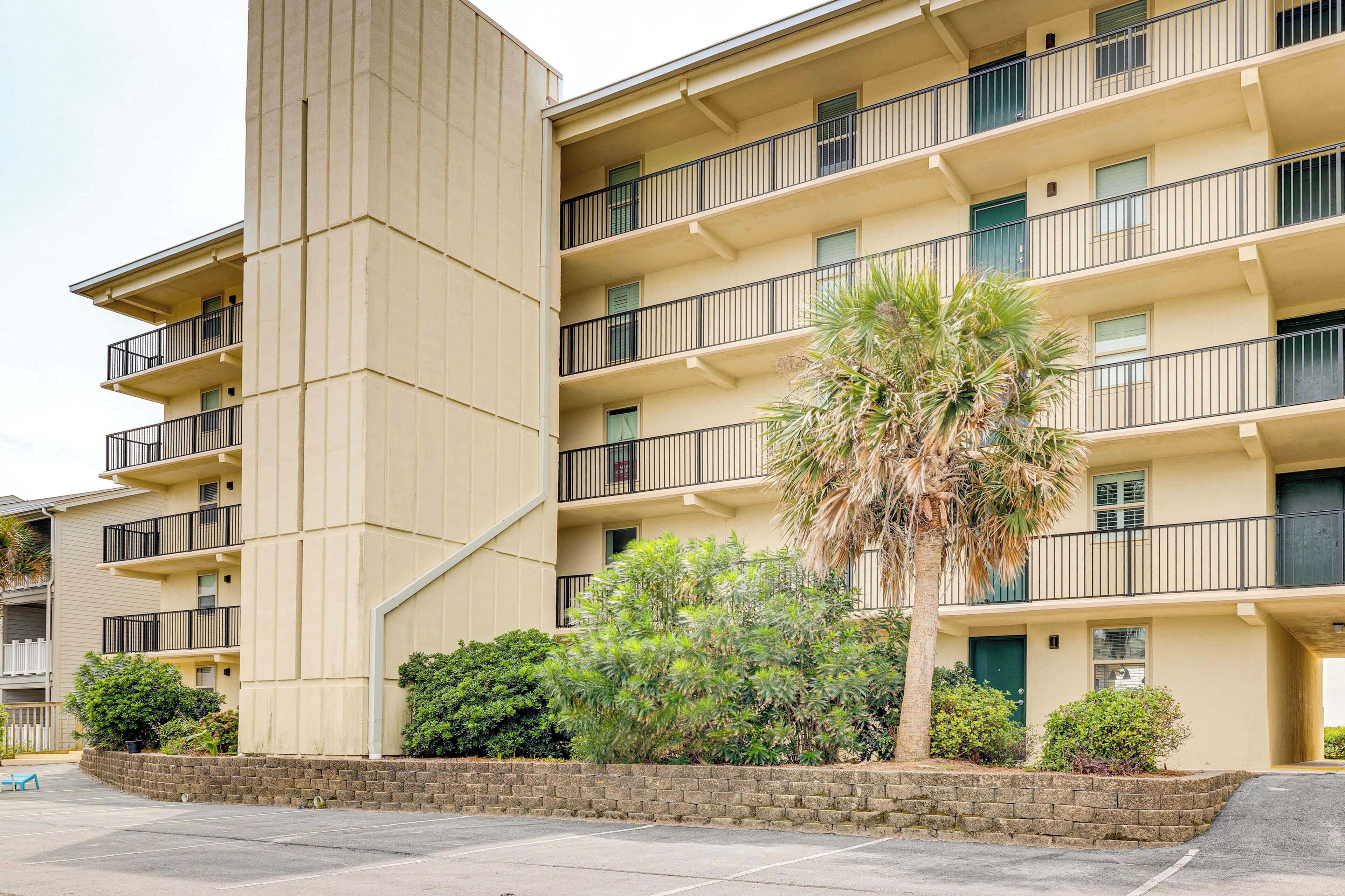 A multi-story building with balconies, a palm tree, and a brick wall.