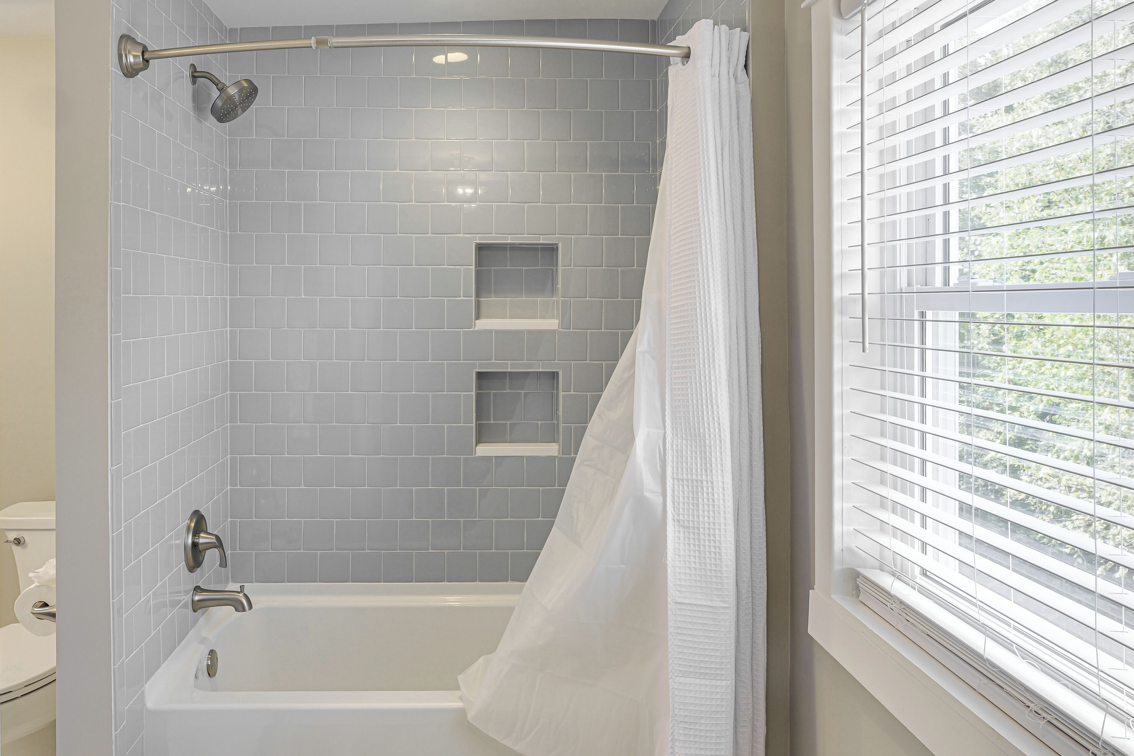 A bathroom with a bathtub, a showerhead, and a window with blinds.