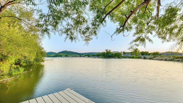 Une jetée en bois s’étendant sur une étendue d’eau calme, entourée d’une végétation luxuriante et de collines lointaines.