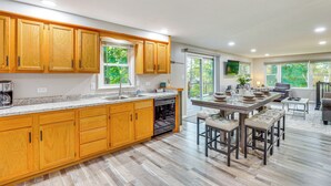 A modern kitchen with wooden cabinets, a built-in dishwasher, and a dining area with stools. - Okee Bay House on Lake Wisconsin w/ Private Dock! (Lodi)