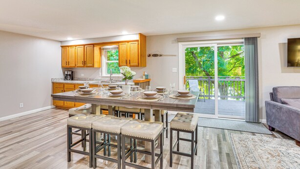 A modern kitchen with wooden cabinets, a large island with bar stools, and a sliding glass door leading to a deck. - Okee Bay House on Lake Wisconsin w/ Private Dock! (Lodi)