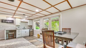 A modern kitchen with wooden cabinets, a dining table with chairs, and a large window with a view of greenery. - Okee Bay House on Lake Wisconsin w/ Private Dock! (Lodi)
