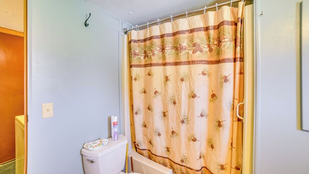 A bathroom with a toilet, a shower curtain with a pine tree pattern, and a towel rack. - Yale Home in the Heart of Pheasant Hunting Country (Yale)