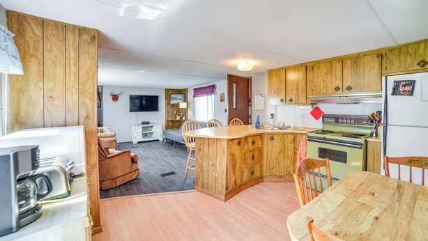 A compact kitchen with wooden cabinets, a dining area with a wooden table and chairs, and a small living space with a sofa and a television. - Yale Home in the Heart of Pheasant Hunting Country (Yale)