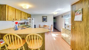 A kitchen with wooden cabinets, a central island with chairs, a refrigerator, and a microwave. - Yale Home in the Heart of Pheasant Hunting Country (Yale)
