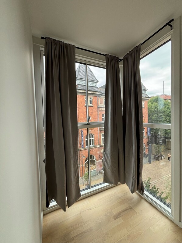 Una habitación con un ventanal grande, cortinas marrones y piso de madera.