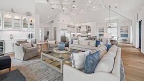 A spacious living area with a high ceiling, modern furniture, and a kitchen in the background.