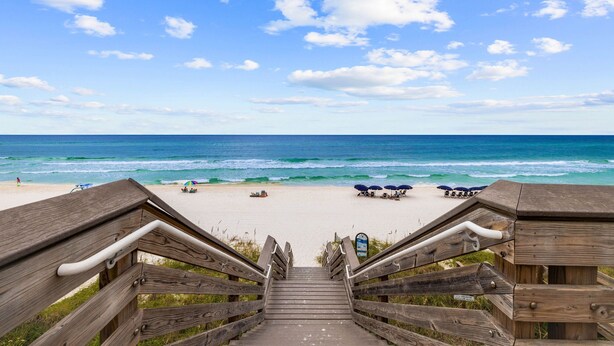 A wooden staircase leading to a beach with umbrellas and beach chairs.