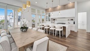 A modern kitchen with white cabinetry, a wooden dining table, and pendant lighting.