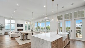 A modern kitchen with a large marble island, wooden cabinets, and pendant lighting.