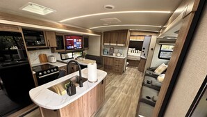 Una cucina compatta con isola centrale, elettrodomestici integrati e TV a schermo piatto.