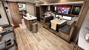 Interni di un camper compatto con angolo cottura, zona salotto e televisore che mostra un menu.