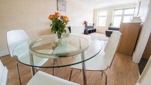 Un comedor moderno con una mesa de vidrio y sillas blancas, un florero con flores y vistas al salón.