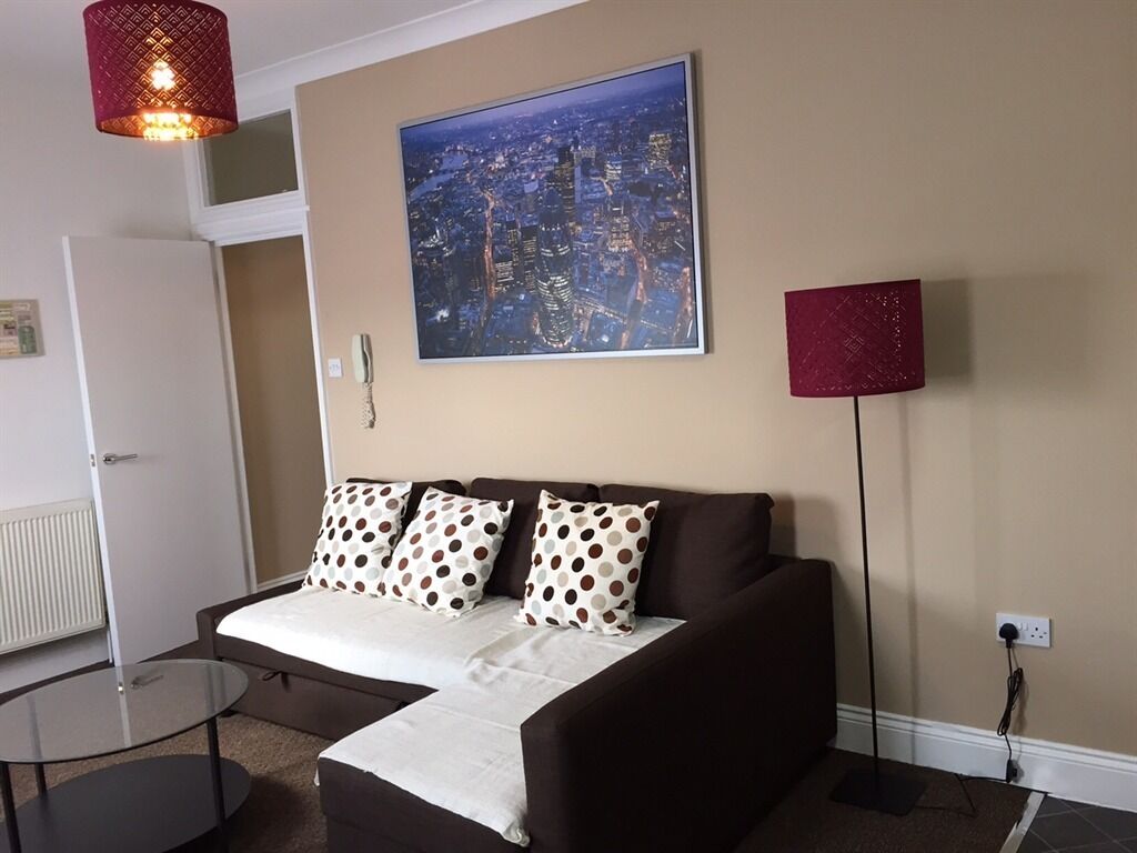 Ein modernes Schlafzimmer mit einem braunen Sofa, einem Stadtbild, einer roten Stehlampe und einem Glastisch.