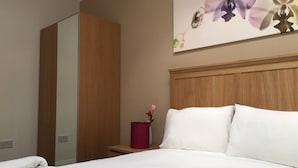 Habitación de hotel con cama, cabecera de madera, mesita de noche con un florero y un espejo grande.