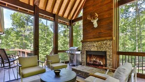 A covered outdoor seating area with stone fireplace, wooden beams, and a deer head decoration. - Francis Oaks by Mountain Oasis | Luxury Cabin in Coosawattee River Resort (Ellijay)