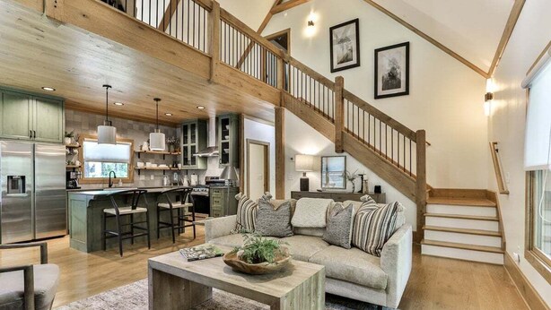 A spacious living area with a wooden staircase, a kitchen with a bar, and a large sofa with cushions. - Francis Oaks by Mountain Oasis | Luxury Cabin in Coosawattee River Resort (Ellijay)