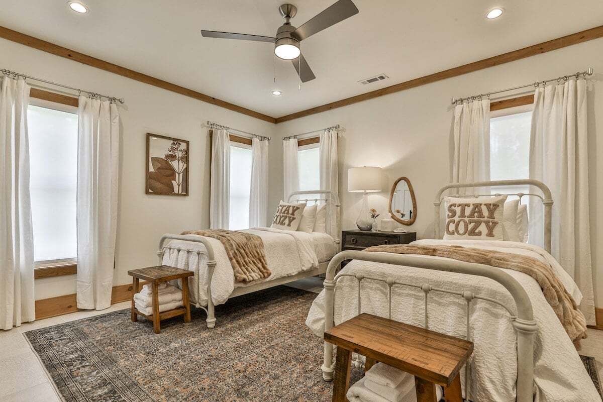 A bedroom with two beds, a ceiling fan, a rug, and a bedside table.
