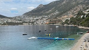 Un pueblo costero con aguas cristalinas, barcos y una playa de arena con sombrillas.