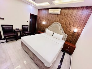A modern hotel room with a large bed, a wooden accent wall, and a ceiling light fixture. - Blue Moon Continental (Islamabad)