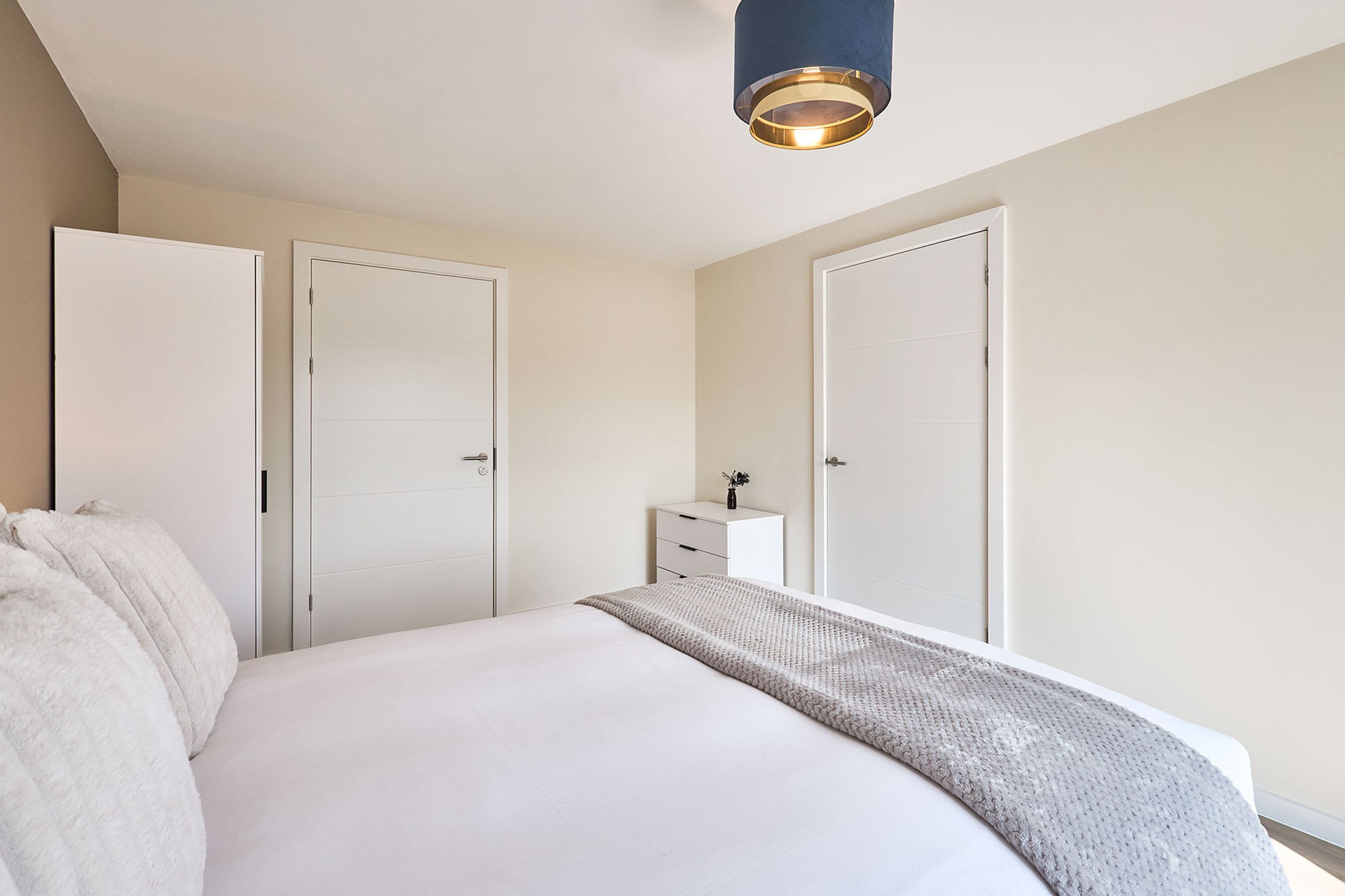 Ein Schlafzimmer mit einem großen Bett, zwei weißen Türen, einem Nachttisch mit Lampe und einer Deckenleuchte.