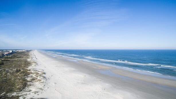A wide beach with a clear sky, a sandy shore, and buildings in the distance. - Seaside Haven Stylish Condo 3 Pools New Rental (St. Augustine)