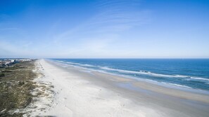 A wide beach with a clear sky, a sandy shore, and buildings in the distance. - Seaside Haven Stylish Condo 3 Pools New Rental (St. Augustine)