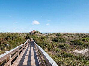 A wooden boardwalk leading to a building with a red roof, surrounded by dense vegetation and a clear blue sky. - Seaside Haven Stylish Condo 3 Pools New Rental (St. Augustine)