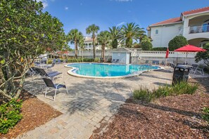 A swimming pool with lounge chairs and a red umbrella, surrounded by palm trees and a building with balconies. - Seaside Haven Stylish Condo 3 Pools New Rental (St. Augustine)