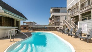 En swimmingpool med ett trädäck, solstolar och en möblerad, överbyggd sittplats.