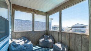En inglasad veranda med träväggar och stora fönster, inredd med två sittpuffar och en randig matta.