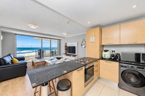 A modern kitchen with a central island, a washing machine, and a view of the ocean.
