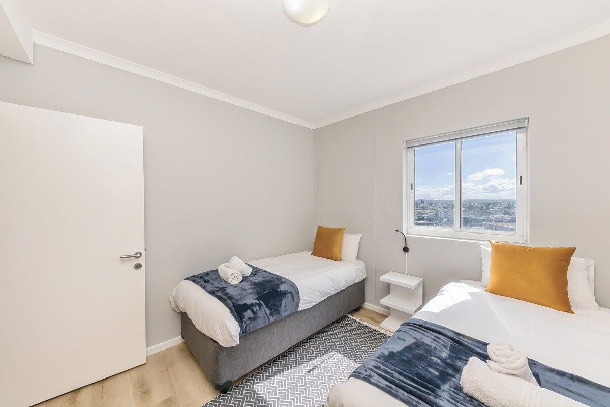 Ein modernes Hotelzimmer mit Bett, Nachttisch, Fenster mit Stadtblick und Tür.