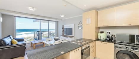 A modern kitchen with a large island, a washing machine, and a view of the ocean.