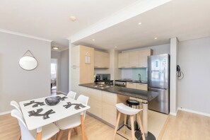 A modern kitchen with a stainless steel refrigerator, a dining area with a white table and chairs, and light wood cabinetry.