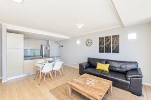 A modern living room with a black leather sofa, a wooden coffee table, and a dining area with white chairs.