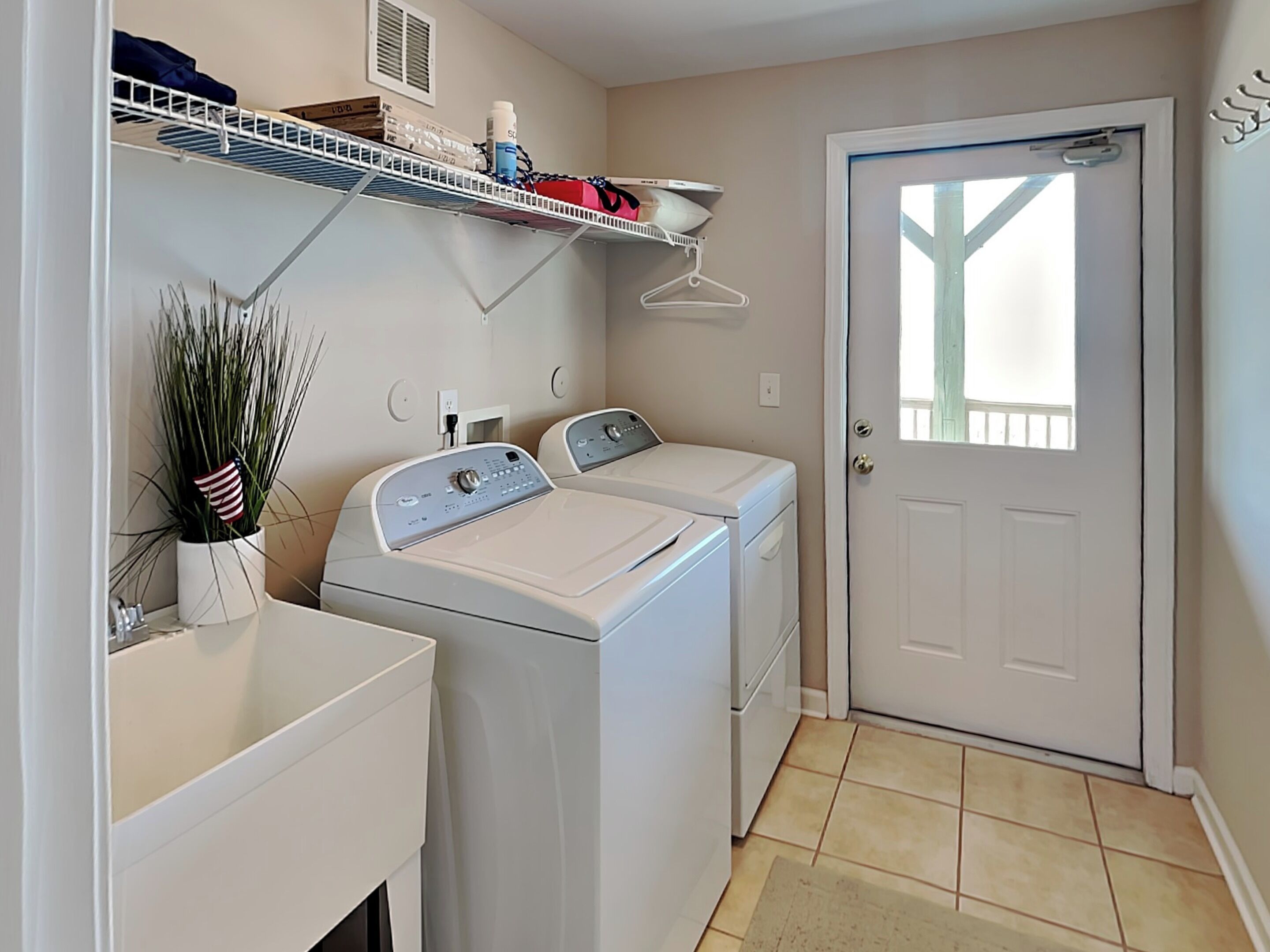 A laundry room with two front-loading washing machines, a drying rack, and a door with a window.