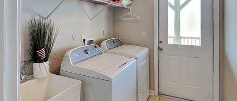 A laundry room with two front-loading washing machines, a drying rack, and a door with a window.