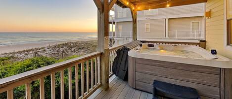 Une terrasse en bois avec un jacuzzi, un banc et une vue sur la plage.