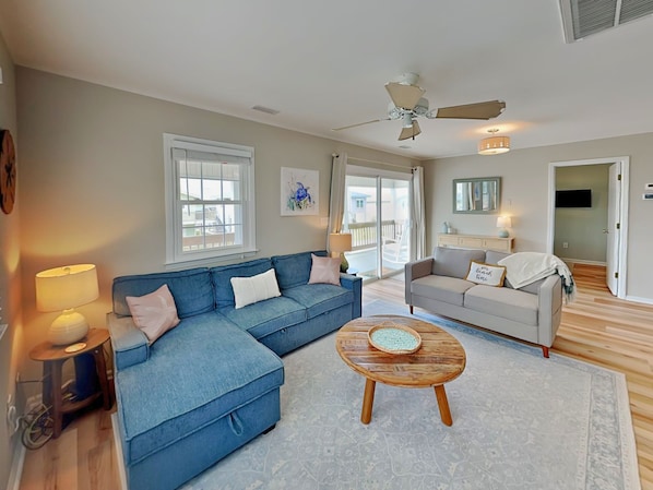 A living room with a blue sectional sofa, a round wooden coffee table, and a ceiling fan.