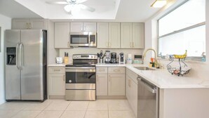 A modern kitchen with stainless steel appliances, light-colored cabinets, and a large window providing natural light. - Walk to the beach 2BR 2BA 1300SF (Riviera Beach)