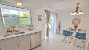 A modern kitchen with white cabinets, a large window, and a dining area with a glass table and chairs. - Walk to the beach 2BR 2BA 1300SF (Riviera Beach)