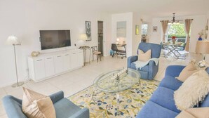 A living room with a sofa, armchairs, a coffee table, and a TV. There is a dining area with a table and chairs. - Walk to the beach 2BR 2BA 1300SF (Riviera Beach)